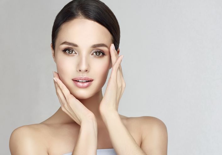 Gorgeous, young, brown haired woman with clean fresh skin is touching the face. Light smile on the perfect face. Facial treatment, cosmetology, beauty technologies and spa.