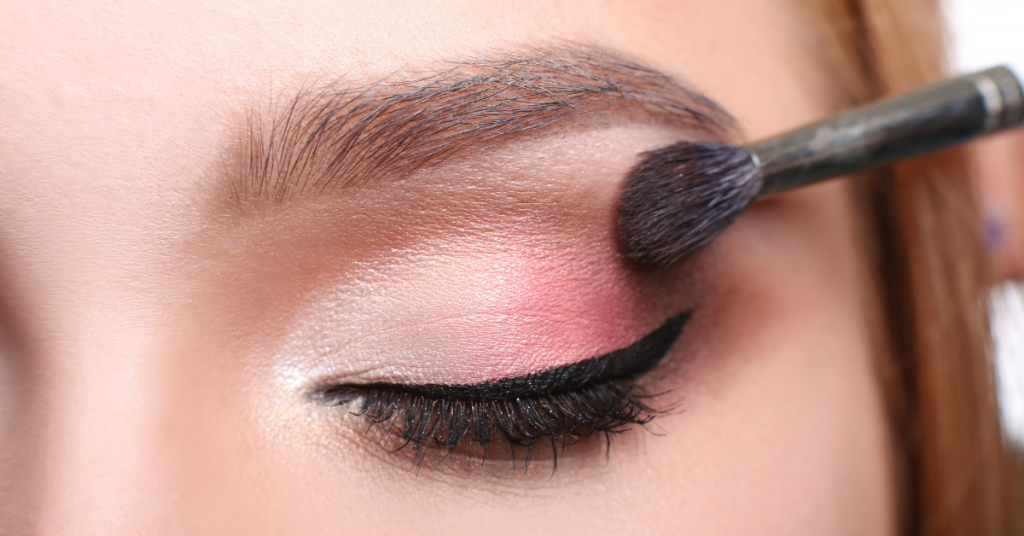 primer plano de un ojo maquillado con sombras en tonos rosas y claros la brocha sigue maquillando el extremo exterior del ojo