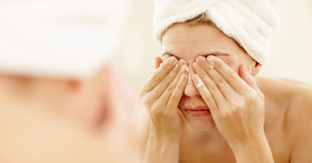 la cara de una chica con una toalla en la cabeza reflejada en unn espejo tiene las manos en los ojos porque se los esta lavando
