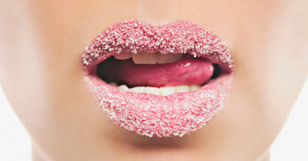 labios con un exfoliante rosa se ven las pequeñas bolas y la lengua que sobre sale por un lado de la boca