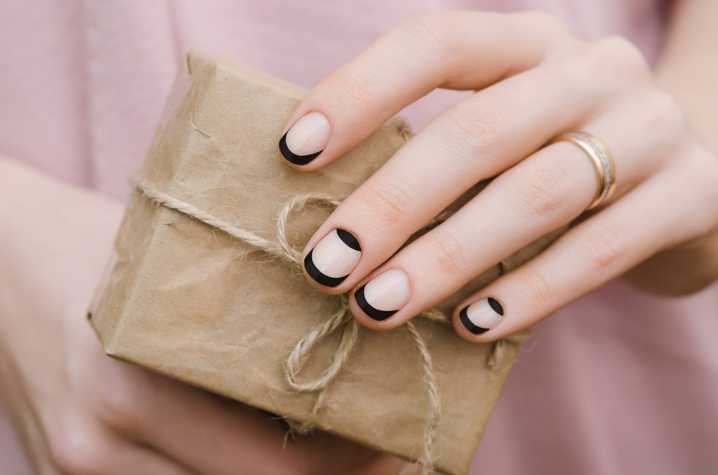 manos de mujer con la manicura francesa en negro hecha sostiene un pequeño paquete envuelto en papel marrón