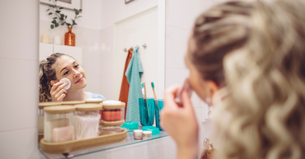 Chica joven se limpia la cara con un algodón frente al espejo de un baño decorado con elementos típicos de esta habitación