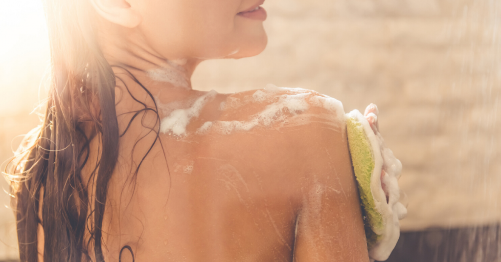  Imagen recortada de una joven desnuda sonriendo mientras se ducha en el baño.