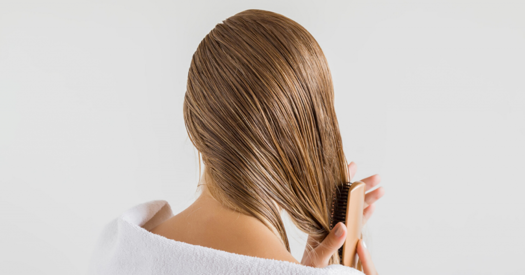 Mujer en la toalla blanca con peine cepillando su cabello rubio mojado después de la ducha sobre el fondo gris. 