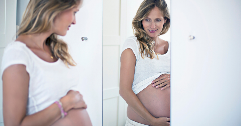 Mujer joven embarazada contempla su barriga en un espejo para ver los tipos de estrías y cómo tratarlas y prevenirlas